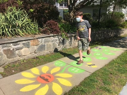 boy playing on a daisy hopscotch spray painted onto the sidewalk