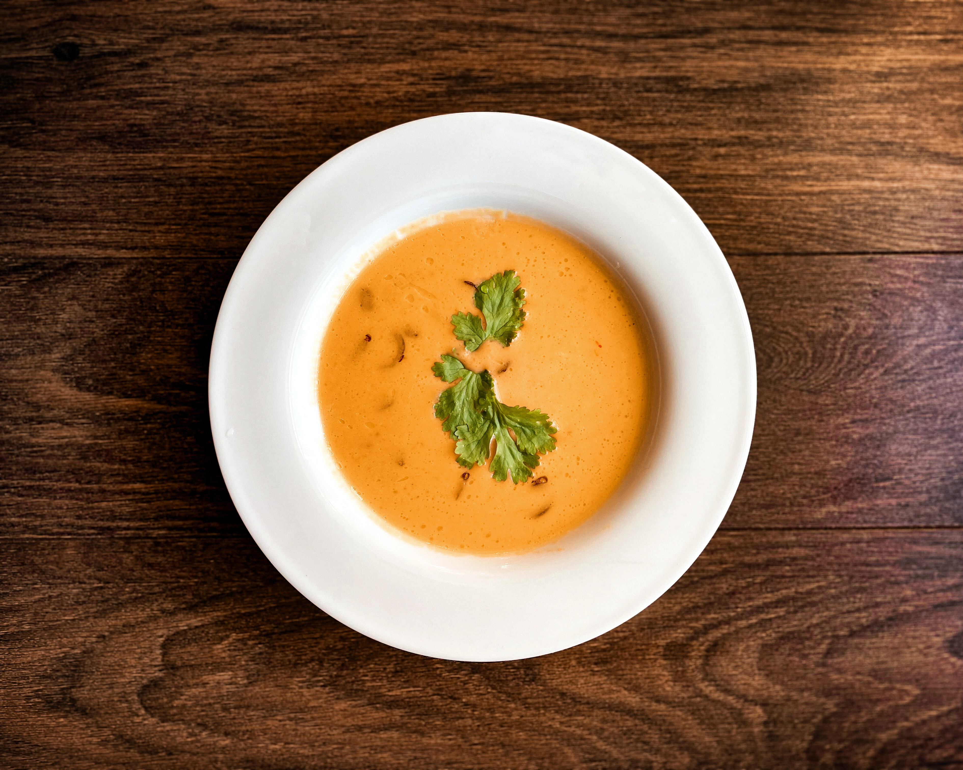 Alt: A dish of butternut squash soup, on a wooden table. Image courtesy of Unsplash, by Jezebel Rose.