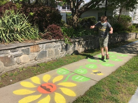 boy jumping on painted daisy hopscotch on sidewalk